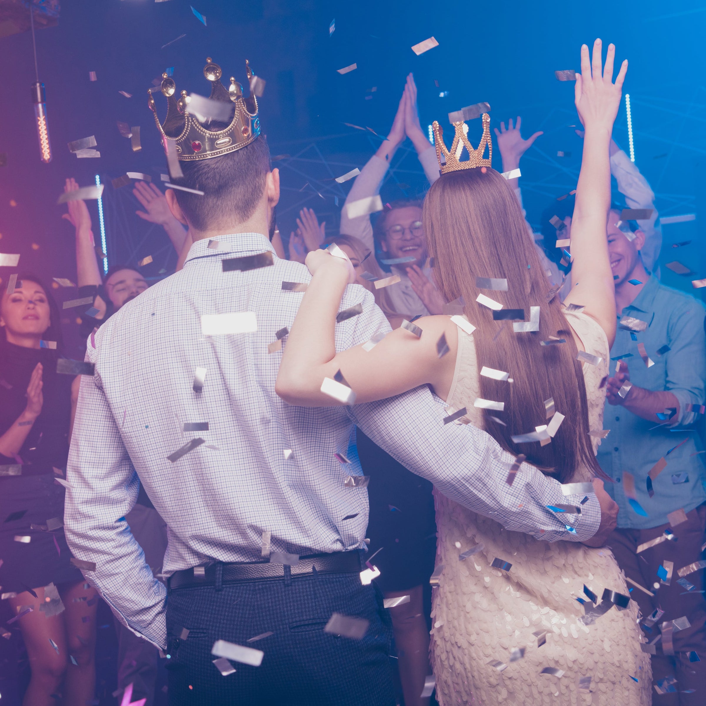 Couple celebrating with crowns on a dance floor surrounded by confetti and people clapping.