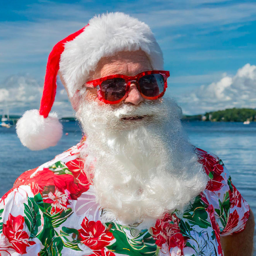 Person wearing a Santa hat and sunglasses with a floral shirt by a lake